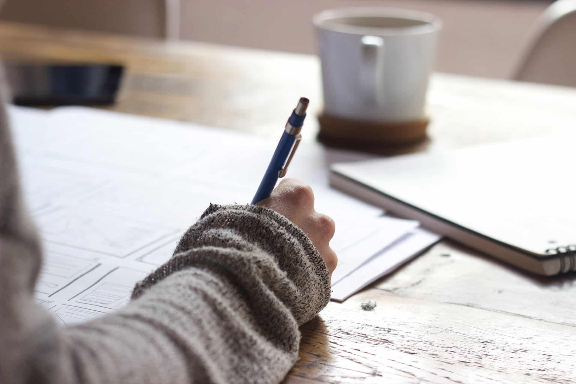 A person writing in a notebook beside a warm drink